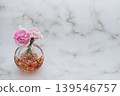 A pink carnation flower and bud in a warm-colored spherical glass vase (left arrangement). A pink carnation flower and bud in a warm-colored spherical glass vase (left arrangement). 139546757