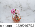 A single pink carnation flower and bud are placed in a warm-colored spherical glass vase (center placement). A single pink carnation flower and bud are placed in a warm-colored spherical glass vase (center placement). 139546758