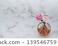 A pink carnation flower and bud in a warm-colored spherical glass vase (arranged on the right). A pink carnation flower and bud in a warm-colored spherical glass vase (arranged on the right). 139546759
