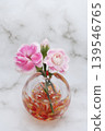 A single pink carnation flower and bud in a warm-colored spherical glass vase (vertical composition). A single pink carnation flower and bud in a warm-colored spherical glass vase (vertical composition). 139546765