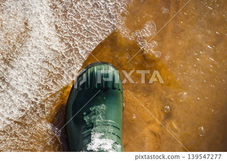 Vibrant green wellington boot crushing crisp ice and splashing into chilly stream water during a brisk outdoor adventure Vibrant green wellington boot crushing crisp ice and splashing into chilly stream water during a brisk outdoor adventure 139547277