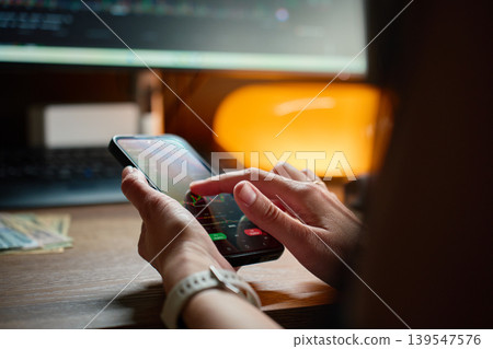 Person using trading app with stock market charts on smartphone at desk Person using trading app with stock market charts on smartphone at desk 139547576