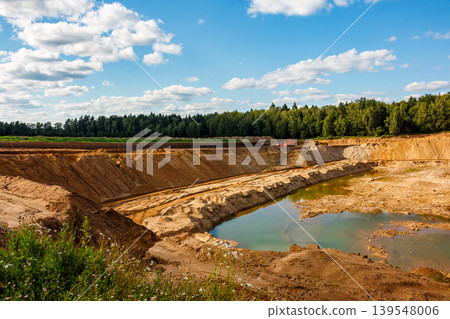 Expansive sand quarry, a huge open-pit, with heavy machinery and a water-filled basin. Earthworks in progress, raw material extraction under blue skies Expansive sand quarry, a huge open-pit, with heavy machinery and a water-filled basin. Earthworks in progress, raw material extraction under blue skies 139548006