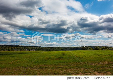Big, puffy clouds fill the bright summer sky above a lush green field. A tranquil country vista, quite peaceful Big, puffy clouds fill the bright summer sky above a lush green field. A tranquil country vista, quite peaceful 139548036