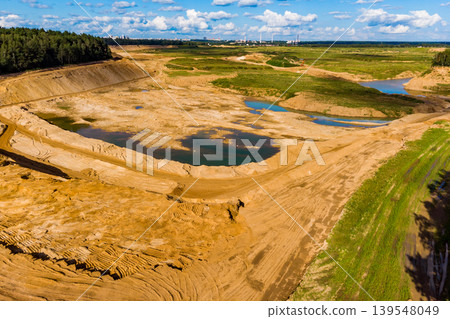Expansive sand quarry, a major open-pit mine, revealing significant earthworks and water pockets, set against a distant urban backdrop Expansive sand quarry, a major open-pit mine, revealing significant earthworks and water pockets, set against a distant urban backdrop 139548049