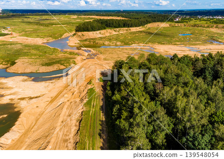 Extensive sand pit excavation, an open-cast mine, alongside a verdant woodland. Reflective pools dot the landscape 139548054