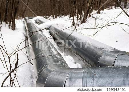 Ground heating pipes in a snowy winter forest. Industrial infrastructure blends with nature. Cold season energy supply. Essential utilities in harsh weather Ground heating pipes in a snowy winter forest. Industrial infrastructure blends with nature. Cold season energy supply. Essential utilities in harsh weather 139548491