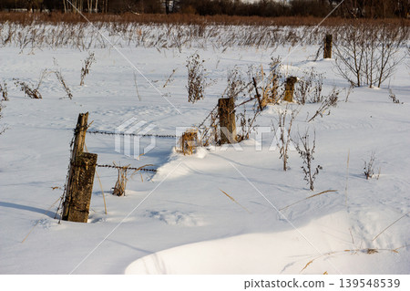 Snow-dusted field, rustic barbed wire fence posts, and dormant winter flora under a crisp clear sky. A tranquil, frosty rural scene Snow-dusted field, rustic barbed wire fence posts, and dormant winter flora under a crisp clear sky. A tranquil, frosty rural scene 139548539