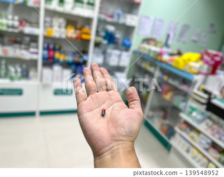 a medicine capsule on a palm with blurry pharmacy shelves background. Concept of healthcare, pharmaceutical treatment, medical prescription, and drug dosage in drug store setting a medicine capsule on a palm with blurry pharmacy shelves background. Concept of healthcare, pharmaceutical treatment, medical prescription, and drug dosage in drug store setting 139548952
