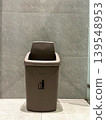 plastic trash bin with swing lid and keep clean icon. Dustbin placed against marble tile wall in public building. Concept of waste disposal, hygiene, and environmental cleanliness 139548953