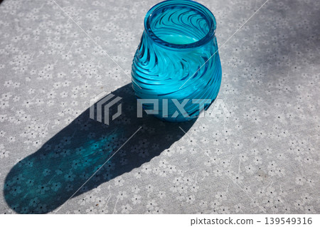 Blue Glass Vase On Patterned Tablecloth With Sunlight Shadow Blue Glass Vase On Patterned Tablecloth With Sunlight Shadow 139549316