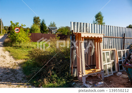 Ornate wooden window casing and old frames lean against a corrugated fence in a rustic village. Rural construction debris or discarded architectural elements 139550212