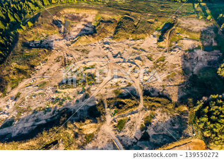 Active sand quarry aerial view. Numerous vehicle tracks crisscross the sandy landscape. Green forest surrounds this industrial site, showcasing resource extraction 139550272