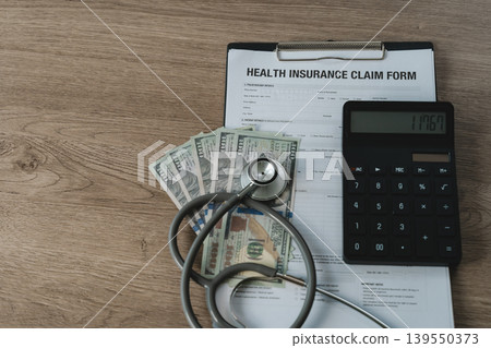Health insurance claim form on a clipboard placed with a stethoscope, US dollar bills, and a calculator as a flat lay on wooden desk, representing medical cost and insurance coverage. Health insurance claim form on a clipboard placed with a stethoscope, US dollar bills, and a calculator as a flat lay on wooden desk, representing medical cost and insurance coverage. 139550373