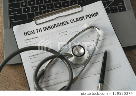 Medical insurance claim form with stethoscope and pen on laptop computer illustrating healthcare administration, patient reimbursement paperwork, and senior medical policy verification workflow. Medical insurance claim form with stethoscope and pen on laptop computer illustrating healthcare administration, patient reimbursement paperwork, and senior medical policy verification workflow. 139550374