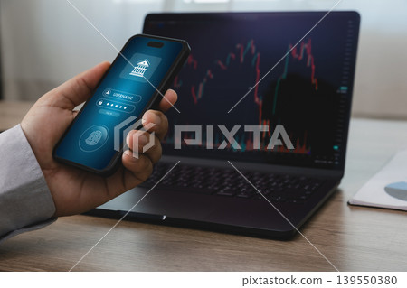 Hand holding smartphone with mobile online banking login screen in front of laptop displaying financial trading chart, suitable for fintech security, digital payment, and online transaction concepts. Hand holding smartphone with mobile online banking login screen in front of laptop displaying financial trading chart, suitable for fintech security, digital payment, and online transaction concepts. 139550380