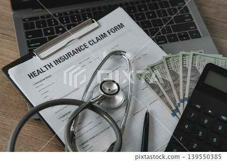 Stethoscope placed on health insurance claim form with cash and calculator on desk, representing medical expense calculation, insurance claim process, healthcare cost management, and financial Stethoscope placed on health insurance claim form with cash and calculator on desk, representing medical expense calculation, insurance claim process, healthcare cost management, and financial 139550385