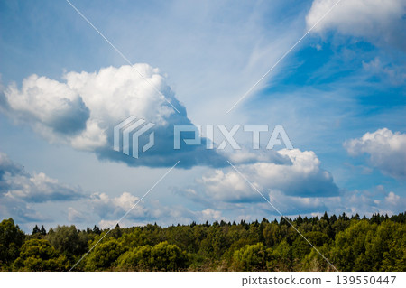 Majestic, billowy clouds drift across a vibrant blue expanse, with a lush forest and green trees grounding the view below. Nature's beauty Majestic, billowy clouds drift across a vibrant blue expanse, with a lush forest and green trees grounding the view below. Nature's beauty 139550447