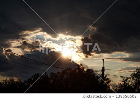 Majestic sunlight pierces through stormy clouds, creating a dramatic sky at dusk. Golden rays peek through dark, thick cumulonimbus 139550502