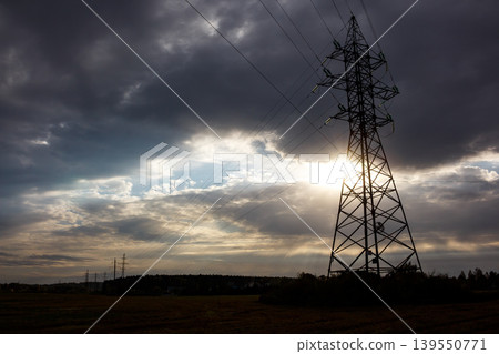 Monolithic pylon, a silent sentinel of power, silhouetted against a dramatic, sun-kissed, cloudy sky, connecting the world with vital energy lines Monolithic pylon, a silent sentinel of power, silhouetted against a dramatic, sun-kissed, cloudy sky, connecting the world with vital energy lines 139550771