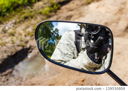 Rearview mirror catches a camouflaged shutterbug, gloved hands on a camera, ready to click. Dusty trail and trees outside Rearview mirror catches a camouflaged shutterbug, gloved hands on a camera, ready to click. Dusty trail and trees outside 139550809