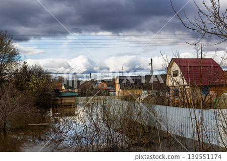 Spring flood inundates a suburban area with small wooden houses, flooded gardens, and metal fences under a dramatic cloudy sky during a gloomy April afternoon in the countryside Spring flood inundates a suburban area with small wooden houses, flooded gardens, and metal fences under a dramatic cloudy sky during a gloomy April afternoon in the countryside 139551174