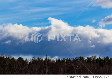 Dramatic clouds loom over a dark forest line under a bright blue sky, hinting at changing weather patterns Dramatic clouds loom over a dark forest line under a bright blue sky, hinting at changing weather patterns 139551176