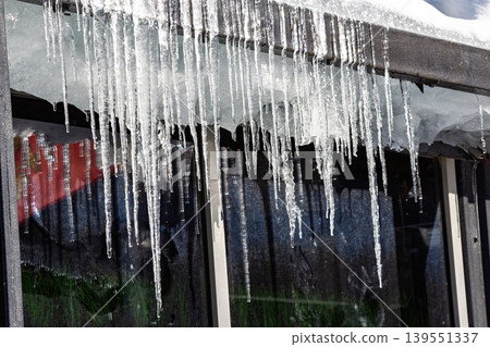 Sparkling melting icicles hang from a roof edge, glistening in sun. Bright, translucent ice formations drip, hinting at the spring thaw. Dynamic winter scene Sparkling melting icicles hang from a roof edge, glistening in sun. Bright, translucent ice formations drip, hinting at the spring thaw. Dynamic winter scene 139551337