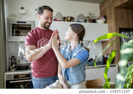 Father and daughter giving high five, standing in kitchen. Father and daughter giving high five, standing in kitchen. 139551397