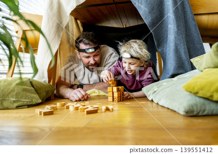 Dad and child building and playing in cozy blanket fort. Dad and child building and playing in cozy blanket fort. 139551412