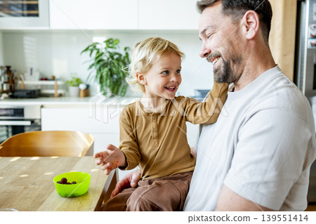 Young child and dad eating healthy snack during playful family moment. Young child and dad eating healthy snack during playful family moment. 139551414