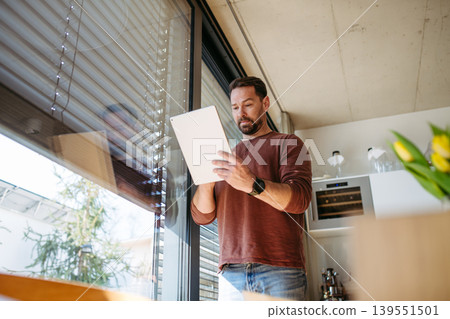 Man using smart home app to control electric window shades indoors. 139551501