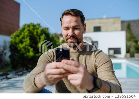 Man using smartphone in backyard and checking messages. 139551504