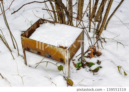 Rusty disposable grill, forgotten in fresh snow. Nature's quiet winter scene marred by human litter, a stark reminder of environmental impact Rusty disposable grill, forgotten in fresh snow. Nature's quiet winter scene marred by human litter, a stark reminder of environmental impact 139551519