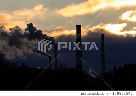 Towering smokestacks spew dense plumes into a dramatic, fiery sky, a stark visual of industrial power and environmental concerns Towering smokestacks spew dense plumes into a dramatic, fiery sky, a stark visual of industrial power and environmental concerns 139551542