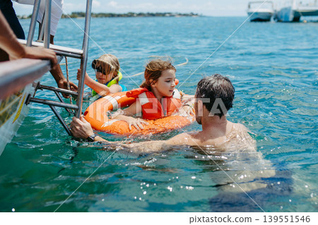 Dad helping child climb from water to boat during summer vacation. Dad helping child climb from water to boat during summer vacation. 139551546