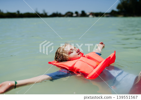 Child floating on water wearing life jacket during summer day. Child floating on water wearing life jacket during summer day. 139551567