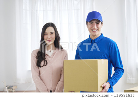 A smiling moving company worker and a woman holding cardboard boxes. A smiling moving company worker and a woman holding cardboard boxes. 139551635