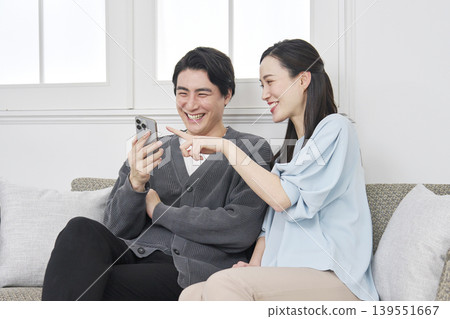 一對夫婦在客廳裡一邊看手機一邊聊天。 139551667
