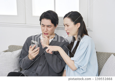 A couple looking at their smartphones in the living room, troubled. A couple looking at their smartphones in the living room, troubled. 139551668