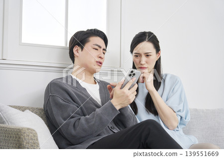 A couple looking at their smartphones in the living room, troubled. A couple looking at their smartphones in the living room, troubled. 139551669