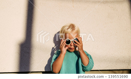 Smiling blond child wearing round sunglasses in warm sunlight. 139551690