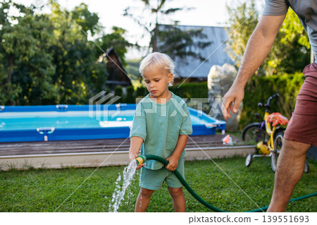 Little boy helping dad in garden, watering plants with hose. Little boy helping dad in garden, watering plants with hose. 139551693