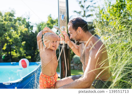 Son and dad using outdoor shower by the pool before swimming. 139551713