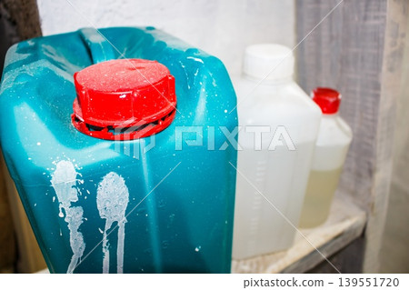 Close-up of a turquoise plastic jerrycan with a bright red dusty cap and white splatter marks, next to translucent bottles in a dim storage area Close-up of a turquoise plastic jerrycan with a bright red dusty cap and white splatter marks, next to translucent bottles in a dim storage area 139551720