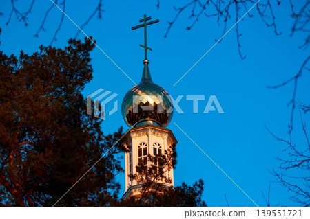 Gleaming orthodox church dome with golden facets catches the last rays of setting sun against deep blue twilight sky framed by dark tree foliage and bare branches Gleaming orthodox church dome with golden facets catches the last rays of setting sun against deep blue twilight sky framed by dark tree foliage and bare branches 139551721