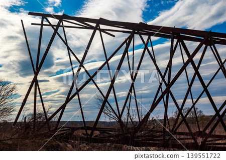Silhouetted against a dramatic spring sky, the rusty metal structure of a dismantled power line pylon dominates the frame, suggesting industrial decay or removal Silhouetted against a dramatic spring sky, the rusty metal structure of a dismantled power line pylon dominates the frame, suggesting industrial decay or removal 139551722