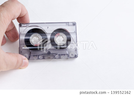 Male hand holding vintage transparent cassette on white background with copy space. Male hand holding vintage transparent cassette on white background with copy space. 139552162