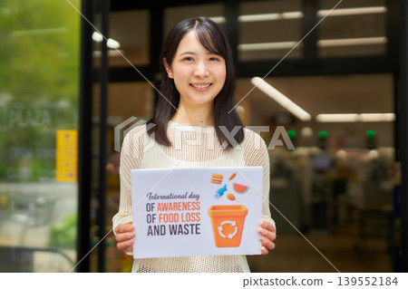 一位年輕女子在超市前舉著一塊關於食物浪費的標語牌。 139552184