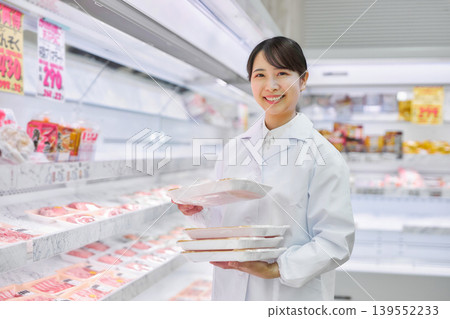一位身穿白大褂的年輕女子正在超市整理肉類。 139552233